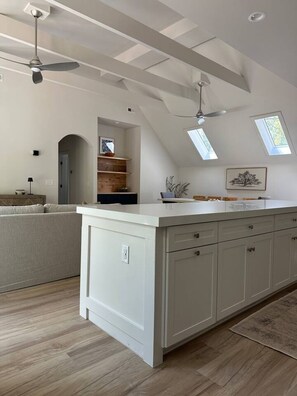 A modern kitchen with a central island, pendant lighting, skylights, and a view of the living area. - Gatehouse at Hawkins (Hurdle Mills)