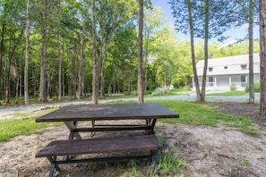 Uma mesa de piquenique numa área arborizada, com um edifício ao fundo.