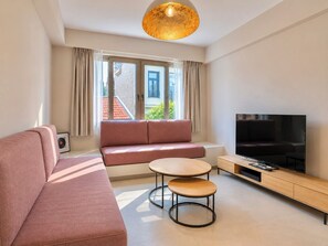 Ein modernes Wohnzimmer mit Sofa, Fernseher, Couchtisch und Pendelleuchte.