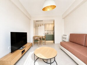 Ein modernes Wohnzimmer mit Flachbildfernseher, einem runden Holztisch, einem braunen Sofa und einer Küche im Hintergrund.