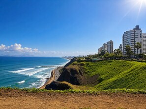 Ein Küstenblick mit Strand, Meereswellen und einer Stadtlandschaft mit Hochhäusern.