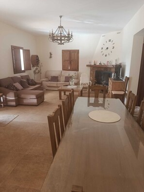 Ein Wohnzimmer mit einer Couch, einem Esstisch, einer Kandelaber, einem Kamin und einer Wanduhr.
