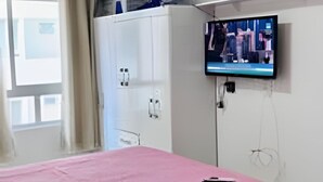 A room with a bed covered in pink, a television mounted on the wall, and a window with curtains. - Conforto em Cabo Branco 2 Qtos - Piscina (João Pessoa)