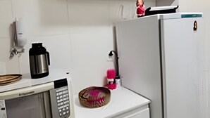 A kitchen with a microwave, a coffee maker, a refrigerator, and a cabinet. - Conforto em Cabo Branco 2 Qtos - Piscina (João Pessoa)