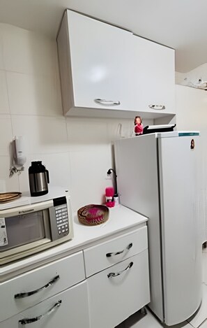 A kitchen with a microwave, a coffee maker, a refrigerator, and a cabinet. - Conforto em Cabo Branco 2 Qtos - Piscina (João Pessoa)