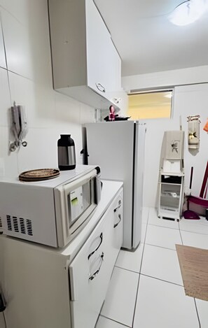 A kitchen with white cabinets, a refrigerator, a microwave, and a coffee maker. - Conforto em Cabo Branco 2 Qtos - Piscina (João Pessoa)