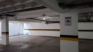 A parking garage with concrete pillars, a no parking sign, and a visible exit sign. - Conforto em Cabo Branco 2 Qtos - Piscina (João Pessoa)