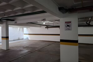 A parking garage with concrete pillars, a no parking sign, and a visible exit sign. - Conforto em Cabo Branco 2 Qtos - Piscina (João Pessoa)