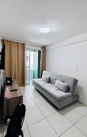 A modern living room with a sofa, a desk, and a television. - Conforto em Cabo Branco 2 Qtos - Piscina (João Pessoa)