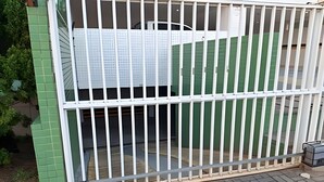 A gated area with a metal fence, a green wall, and a paved ground. - Conforto em Cabo Branco 2 Qtos - Piscina (João Pessoa)