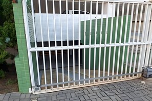 A gated area with a metal fence, a green wall, and a paved ground. - Conforto em Cabo Branco 2 Qtos - Piscina (João Pessoa)