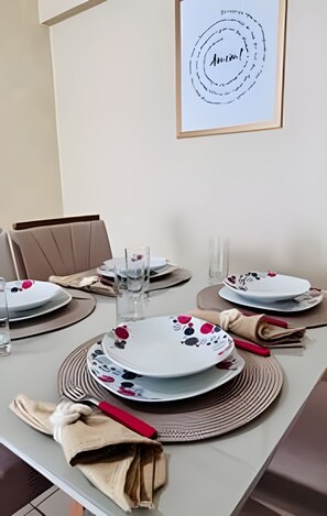 A dining table set with plates, glasses, and cutlery, with a framed artwork above. - Conforto em Cabo Branco 2 Qtos - Piscina (João Pessoa)