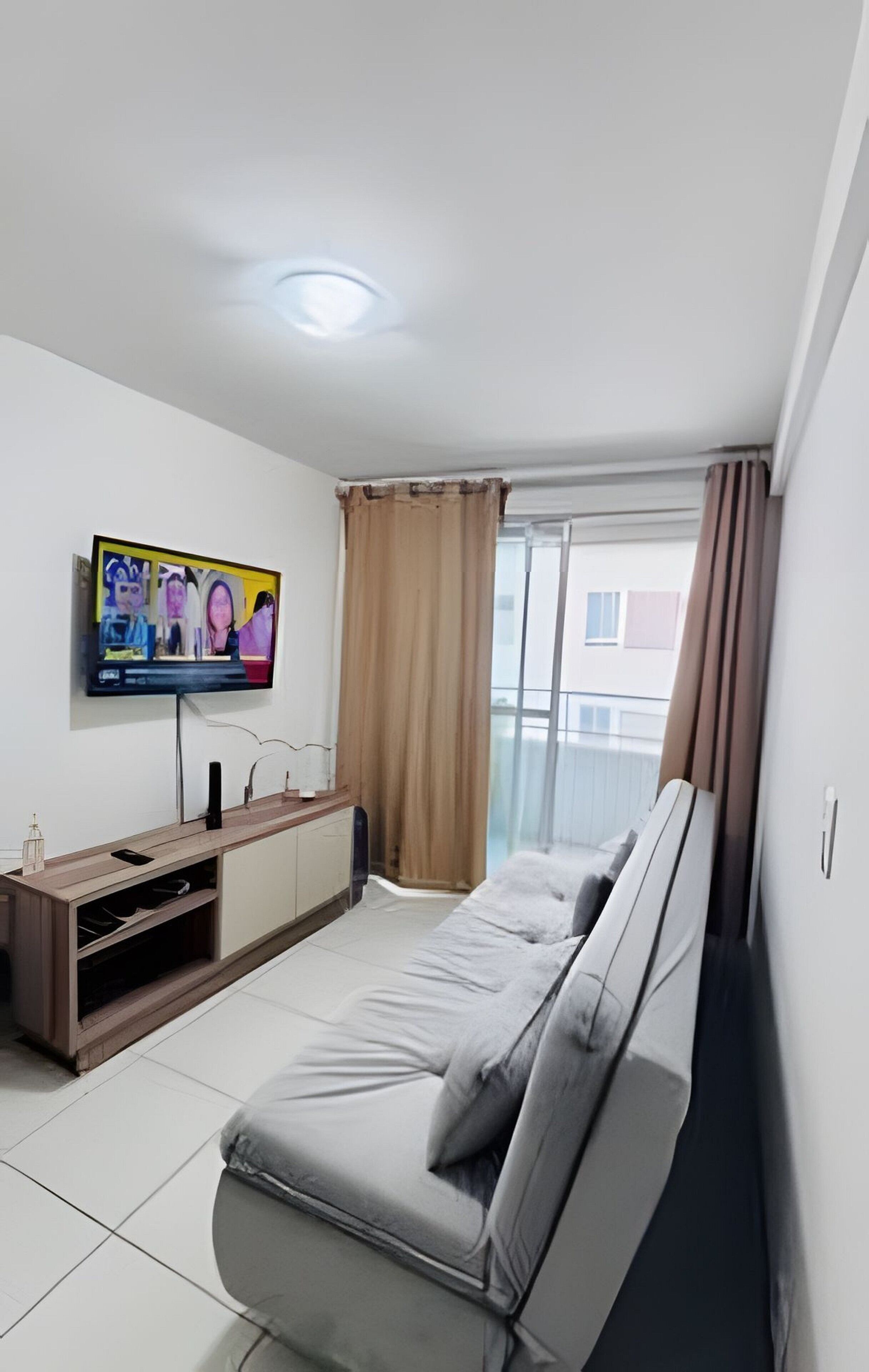 A modern bedroom with a bed, a TV mounted on the wall, and a window with curtains.