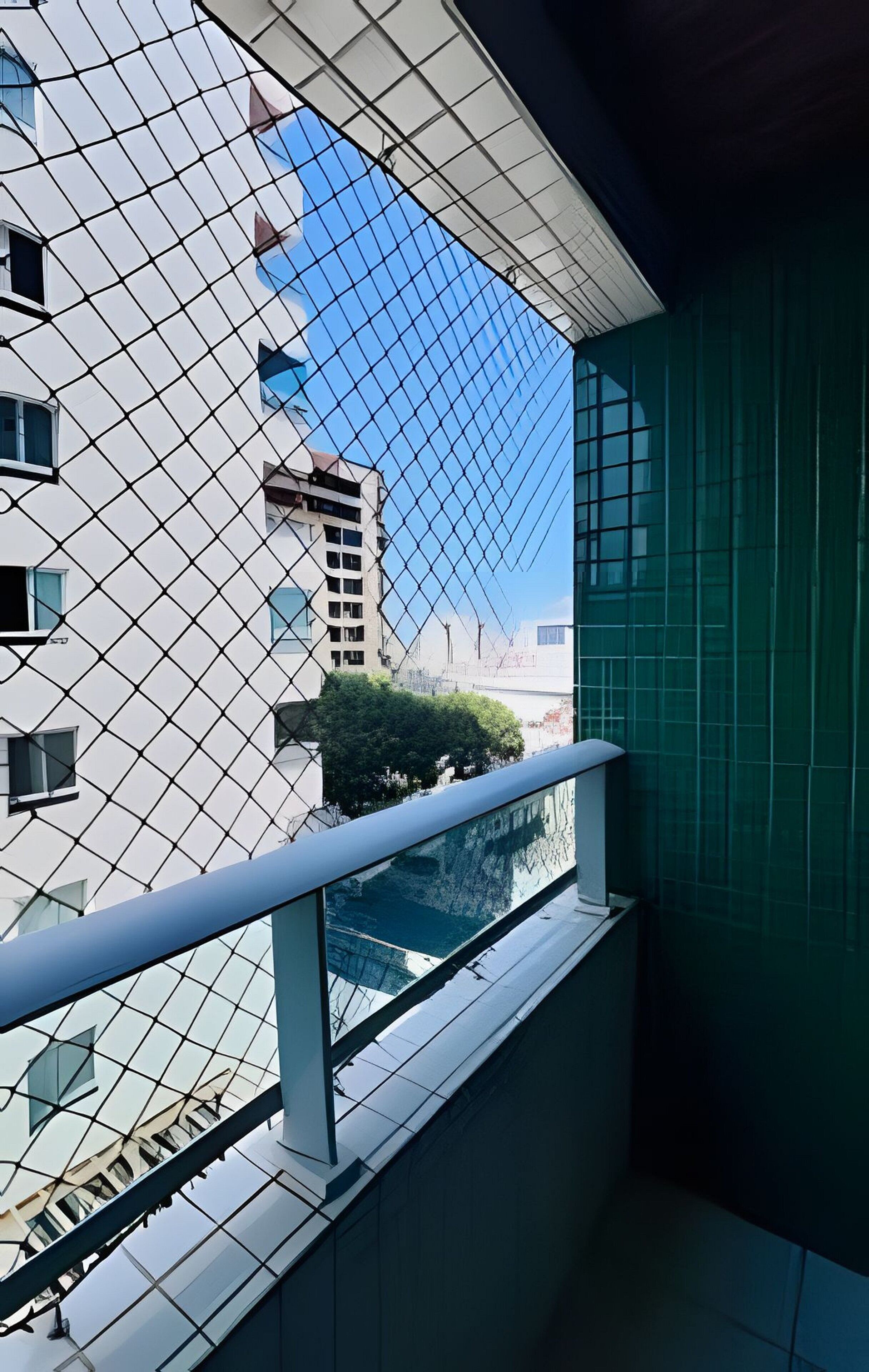 A modern building with a glass facade, a balcony with a metal railing, and a clear blue sky in the background.
