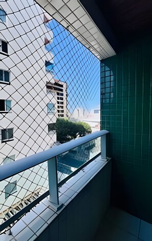 Un bâtiment moderne doté d’une façade en verre, d’un balcon avec une rambarde en métal et, en arrière-plan, d’un ciel bleu azur.