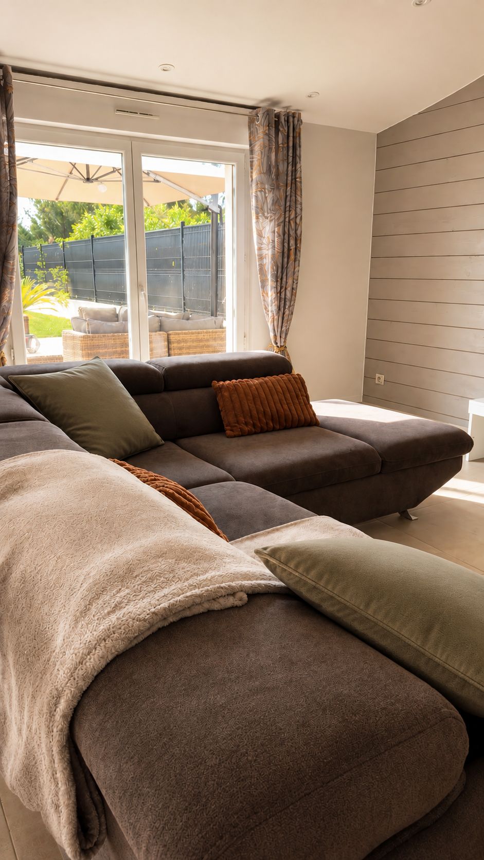 A modern living room with a sectional sofa, a large window with curtains, and a view of the outdoors.
