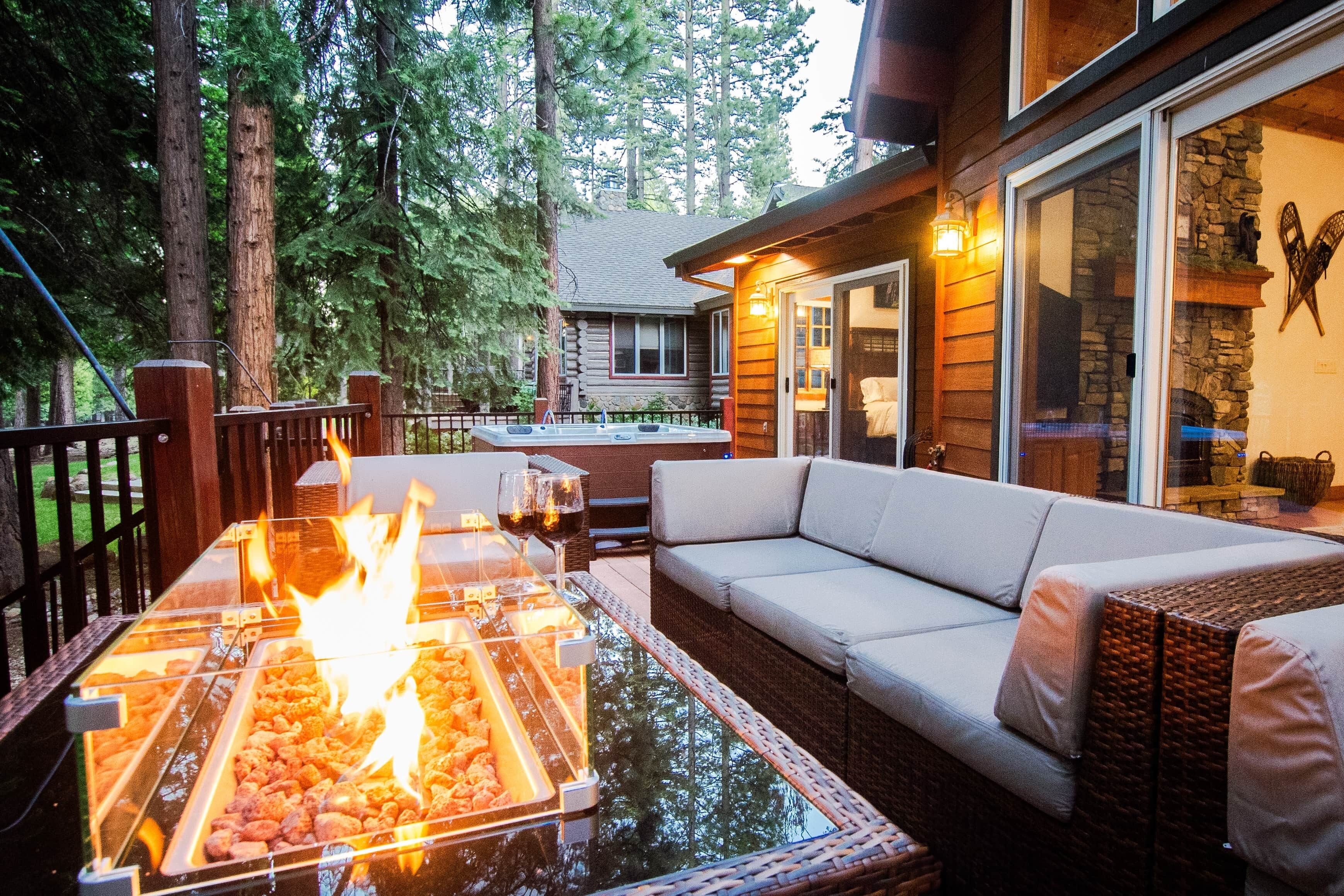 An outdoor seating area with a glass-top table and a fire feature, a sofa, and a stone wall.