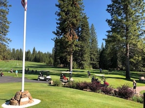 Un campo de golf con un mástil de bandera, árboles y carritos de golf.