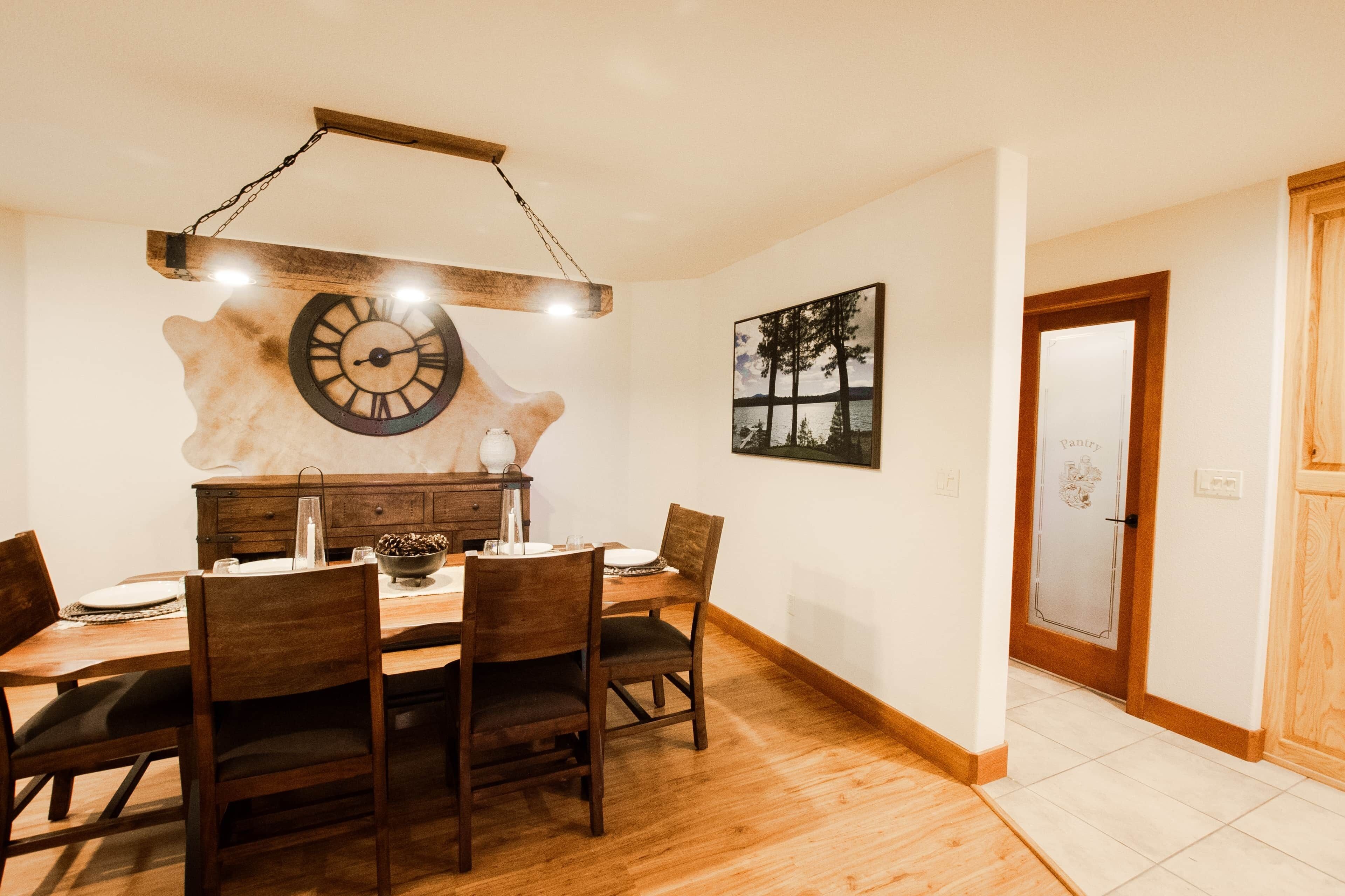 A dining area with a wooden table, chairs, a clock, and a painting on the wall.