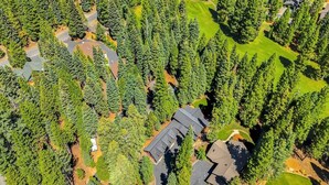 Eine Luftaufnahme eines Wohngebiets mit dichten Nadelbäumen, einem Golfplatz und Häusern mit dunklen Dächern.