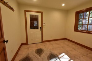 A room with a white door, a window with a view of trees, and a tiled floor.