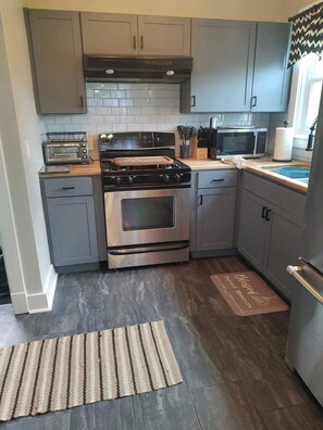 A modern kitchen with grey cabinets, a stainless steel stove, a microwave, and a toaster. - Perfect 3-bedroom house in the heart of Mt. Washingston (Pittsburgh)