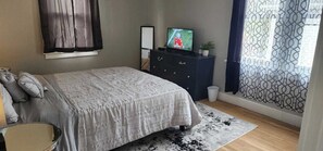 Een slaapkamer met een bed, een dressoir, een televisie en een raam met gordijnen.