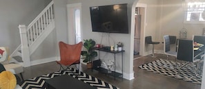 A living room with a staircase, a flat-screen TV, a dining area with chairs, and a patterned rug. - Perfect 3-bedroom house in the heart of Mt. Washingston (Pittsburgh)