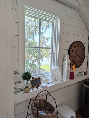 A room with a large window, a wall clock, a small sign, a basket, and a white cabinet. - Canoe Club Loft - Dock slip available (Daufuskie Island)
