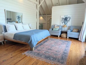 A bedroom with a bed, two armchairs, a rug, and a wall with a decorative piece. - Canoe Club Loft - Dock slip available (Daufuskie Island)