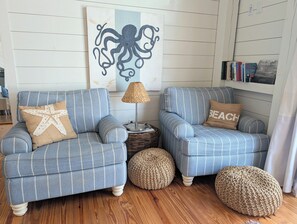 A room with two blue-striped armchairs, a starfish pillow, a woven lamp, and a bookshelf with books. - Canoe Club Loft - Dock slip available (Daufuskie Island)