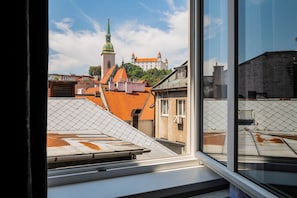 Blick aus einem Fenster auf eine Stadtlandschaft mit einem markanten Kirchturm und einer Burg in der Ferne.