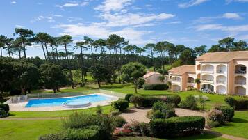 Une piscine entourée de pelouses et d’arbres bien entretenus, avec un bâtiment doté de nombreux balcons et d’un toit recouvert de tuiles.