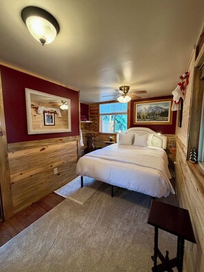 Ein Schlafzimmer mit Bett, Deckenventilator, Fenster mit Blick und einer Holzwand.