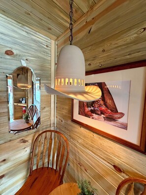 Ein Holzinterieur mit einem Esstisch, Stühlen, einer Hängelampe und einem gerahmten Bild an der Wand.