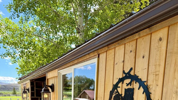 Een houten gebouw met een 'WELCOME'-bord, een bankje en een barbecue voor buiten.