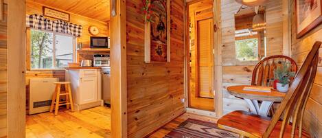 A wooden cabin interior with a kitchen, dining area, and a visible door leading outside.