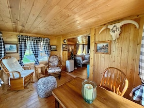 Interior de una cabaña de madera con una mesa de comedor, sillas, una chimenea y un árbol de Navidad.