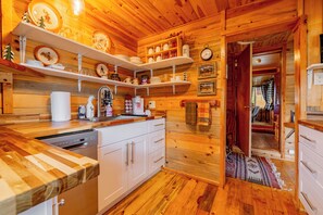 Ein Holzinterieur mit Küchenbereich, weißen Schränken, einem Geschirrspüler und verschiedenen Küchenutensilien auf Regalen.