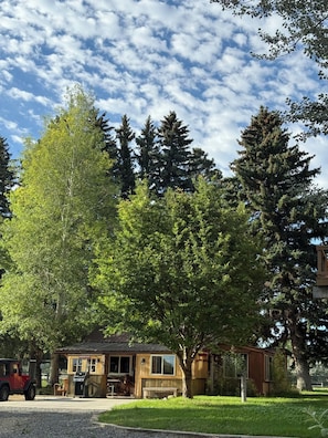 Una cabaña rústica con fachada de madera, un pequeño porche y una zona de barbacoa.