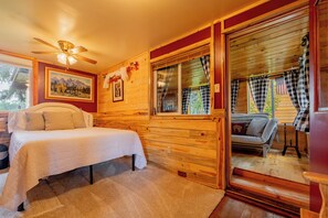 Una habitación acogedora con cama, ventana con cortinas, ventilador de techo y un cuadro en la pared.