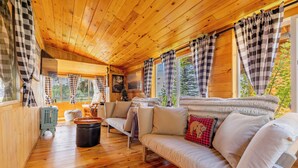 Een gezellig chaletinterieur met een houten plafond, een bank, een tafel en uitzicht op de omgeving.