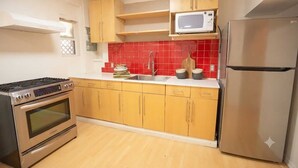 Una cocina con armarios de madera, un refrigerador de acero inoxidable, un microondas, una estufa y un salpicadero de azulejos rojos.