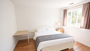 Un dormitorio con cama, mesita de noche, lámpara y ventana con cortinas.
