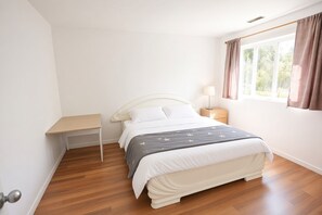 A bedroom with a bed, bedside table, lamp, and window with curtains. - Airport Cozy 2 Bedroom Suite & Separate Entrances & Full kicthen (Richmond)