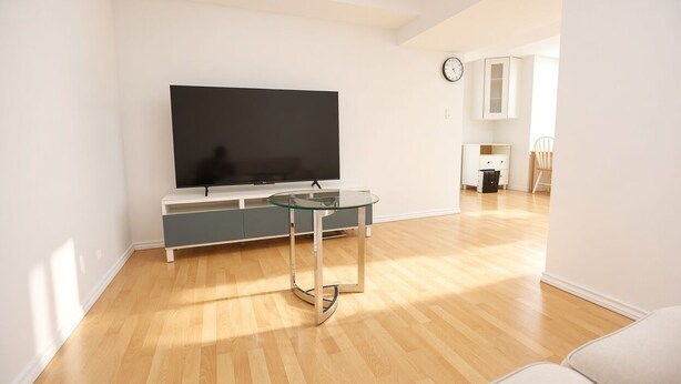 Una sala de estar moderna con televisor de pantalla plana, una mesa de centro de vidrio y una zona de cocina al fondo.