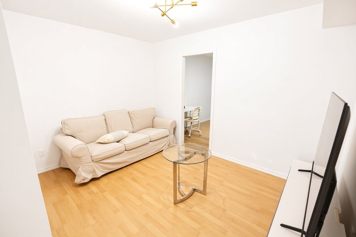 A minimalist living room with a beige sofa, a glass coffee table, and a flat-screen TV.