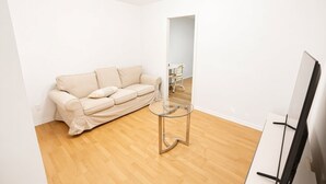 Una sala de estar minimalista con un sofá beige, una mesa de centro de vidrio y un televisor de pantalla plana.