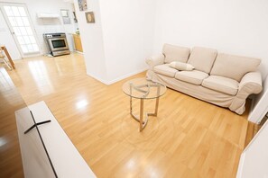 Ein modernes Wohnzimmer mit einem beigefarbenen Sofa, einem Glastisch und Holzboden.