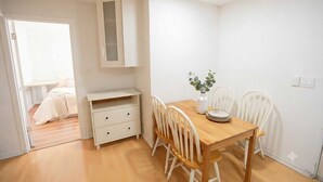 Una habitación con una mesa de comedor de madera, sillas blancas, un mueble pequeño y una puerta blanca que da a otra estancia.